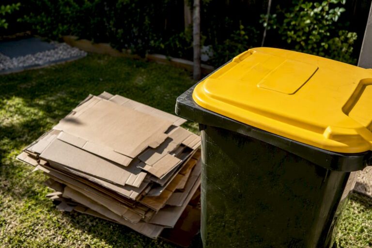 Flattened cardboard stacked beside recycling bin