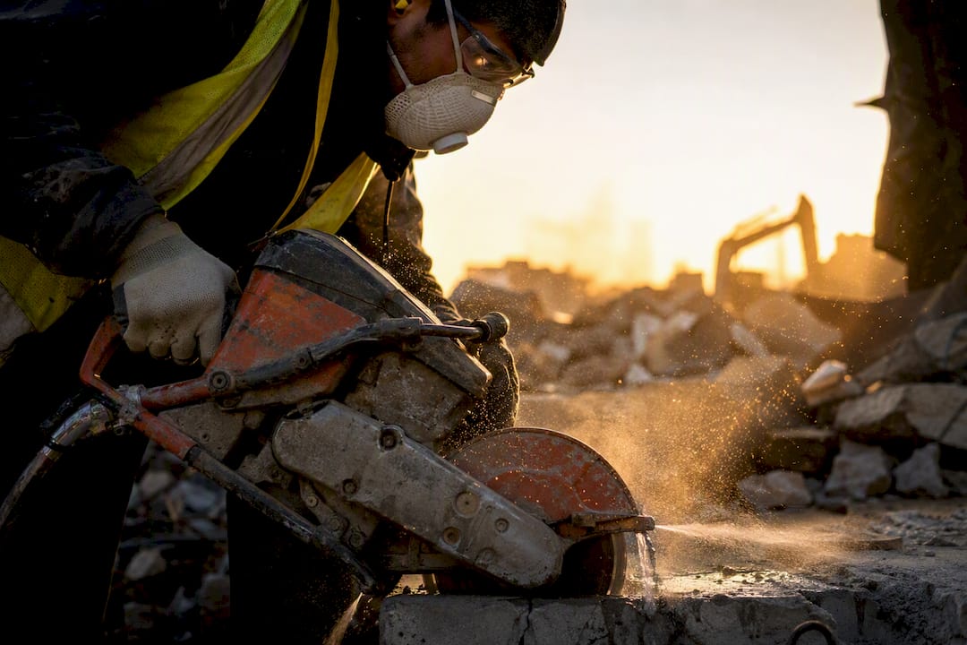 Worker using concrete cutter with dust mask and water spray