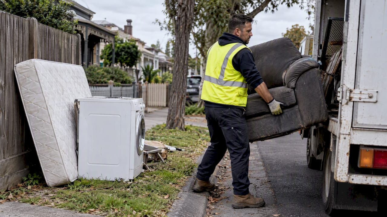 Worker loading bulky rubbish beside a kerbside setout