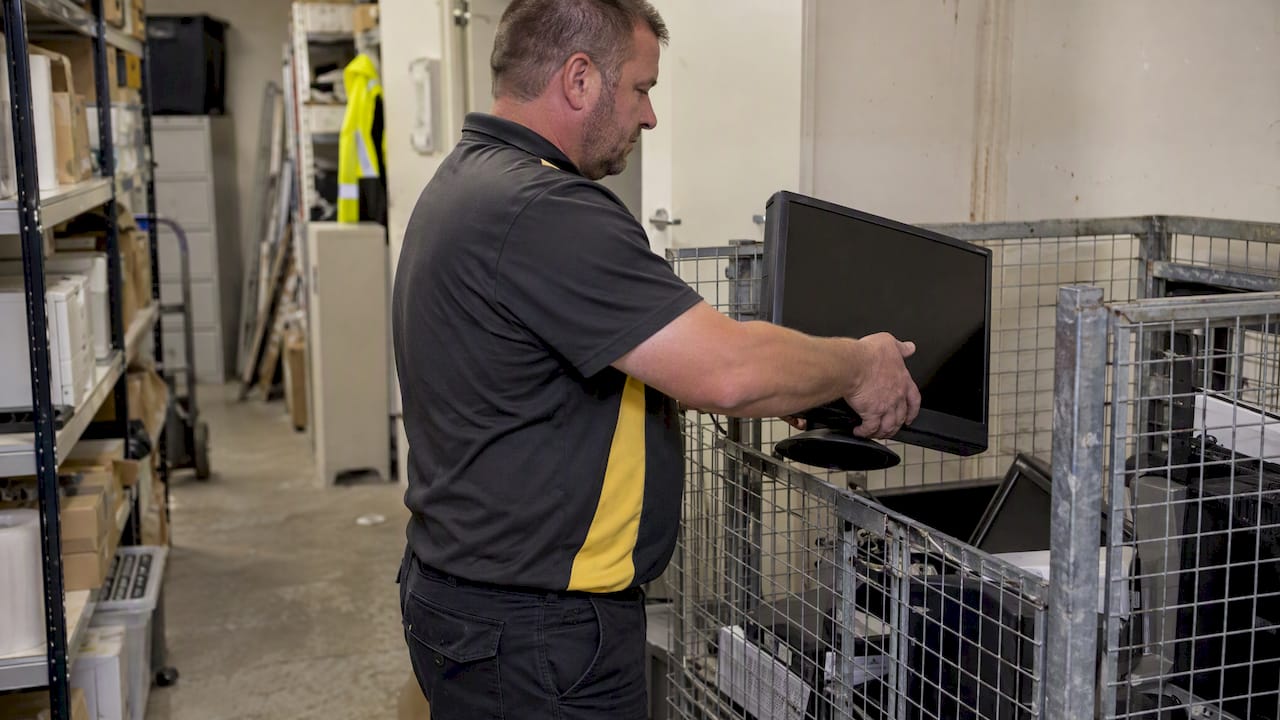 Worker placing an old monitor in e-waste collection